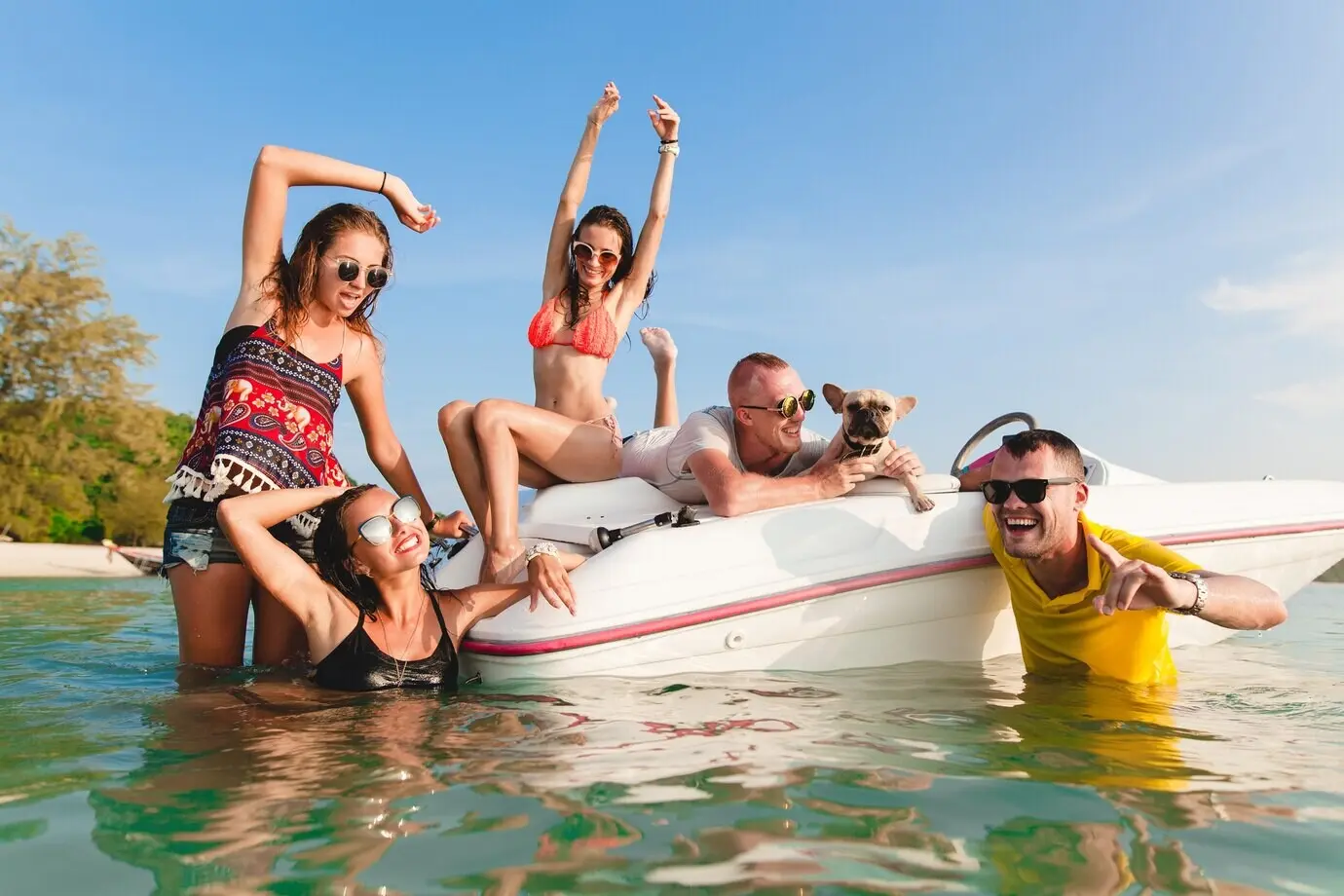 Joyful group of friends on a summer tropical vacation in Thailand, traveling by boat on the sea and partying on the beach; men and women having fun together with positive emotions.