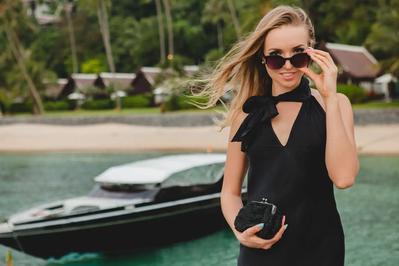 A luxurious, sexy, attractive woman in a black dress and sunglasses posing on a pier at a luxury resort hotel during a summer vacation at a tropical beach.